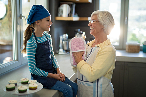 Smiling grandmother and granddaughter with oven gloves in the kitchen