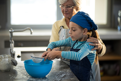 Grandmother assisting granddaughter to sieve the flour in the kitchen