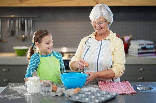 Smiling grandmother showing granddaughter to break eggs in the kitchen