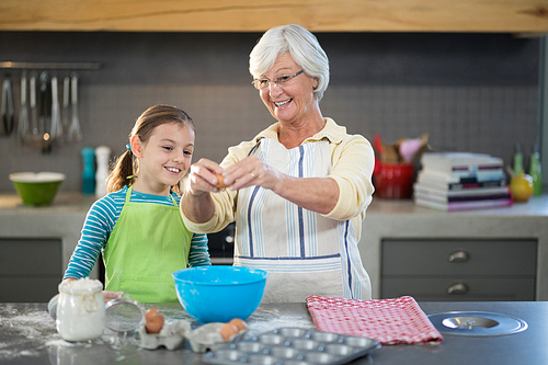 Smiling grandmother showing granddaughter to break eggs in the kitchen