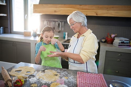 Grandmother showing a cut dough to her granddaughter in the kitchen