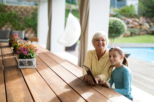 Smiling granddaughter and grandmother sitting in a deck shade with a digital tablet