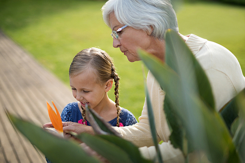 Smiling granddaughter and grandmother looking at a yellow flower on the plant