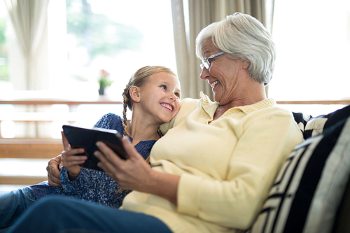 Smiling granddaughter and grandmother using digital tablet on sofa in living room