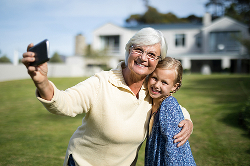 Grandmother and granddaughter taking selfie with mobile phone in garden on a sunny day