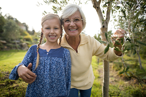 Portrait of smiling granddaughter and grandmother standing together in garden on a sunny day