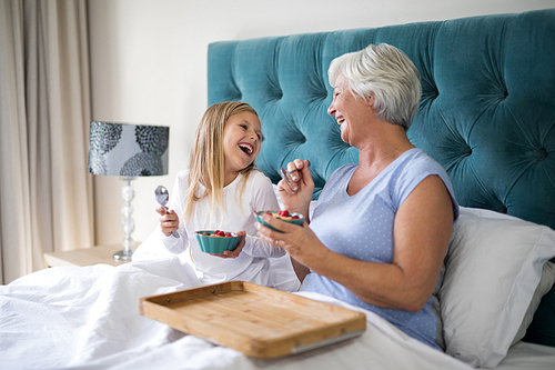 Smiling granddaughter and grandmother interacting while having breakfast on bed