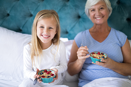 Portrait of smiling granddaughter and grandmother having breakfast on bed