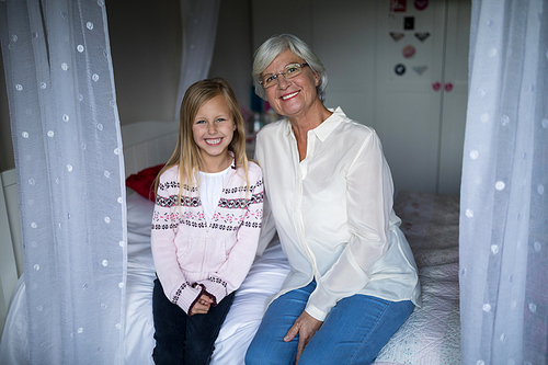 Portrait of smiling grandmother and granddaughter sitting together on bed