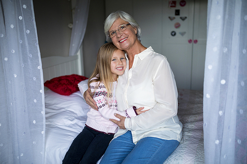 Portrait of smiling grandmother and granddaughter sitting together on bed