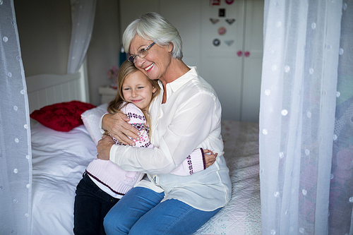 Smiling grandmother and granddaughter embracing each other on bed in bedroom