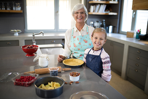Smiling grandmother and granddaughter posing while making pie in the kitchen