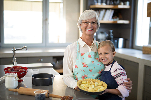 Grandmother and granddaughter posing with fresh cut apples on crust while making apple pie