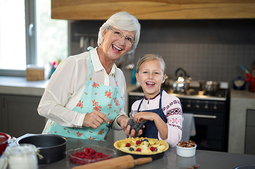 Grandmother and granddaughter posing while adding blue berries to the crust while making apple pie