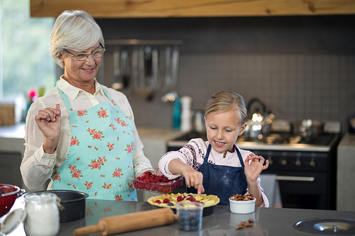 Grandmother and granddaughter adding strawberries to the crust while making apple pie