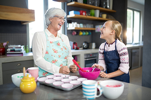 Smiling grandmother and granddaughter looking at each other in the kitchen