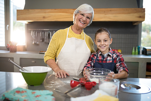 Close-up of smiling grandmother and granddaughter holding a bowl of flour in the kitchen