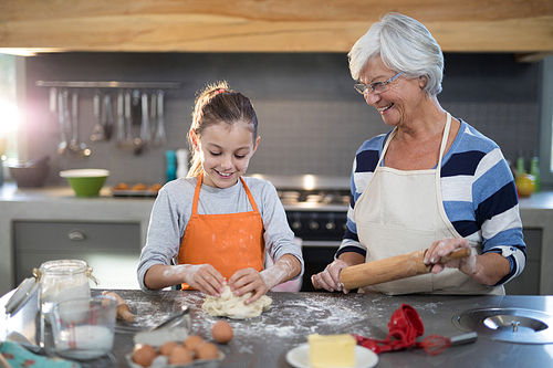 Smiling granddaughter kneading dough while standing with grandmother