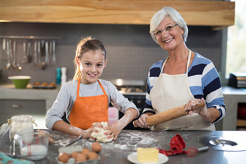 Smiling granddaughter kneading dough while posing with grandmother