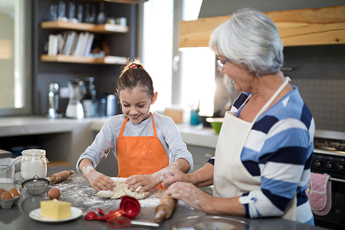 Smiling granddaughter kneading dough while standing with grandmother