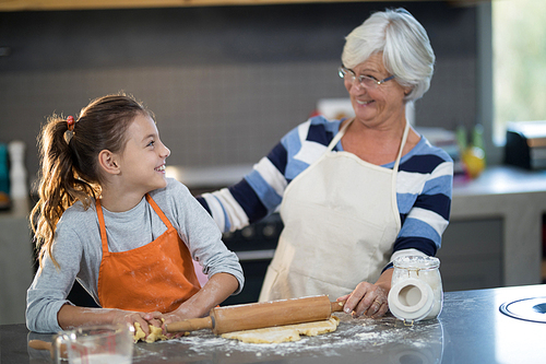Grandmother and granddaughter looking at each other while flattening dough in the kitchen