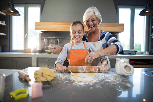 Grandmother helping granddaughter to flatten dough in the kitchen