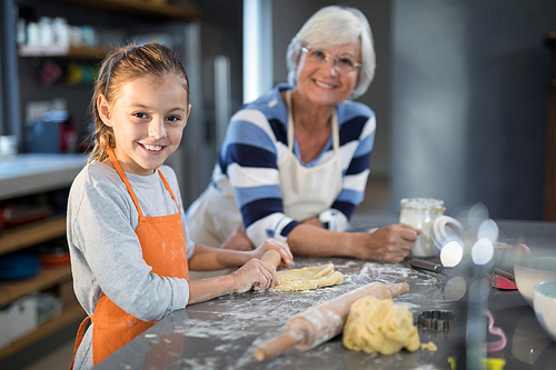 Grandmother and granddaughter posing while flattening dough in the kitchen