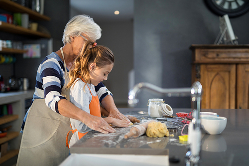Grandmother helping granddaughter to flatten dough in the kitchen