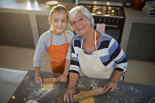 Grandmother and granddaughter posing while flattening dough in the kitchen