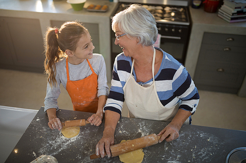 Grandmother and granddaughter looking at each other while flattening dough in the kitchen