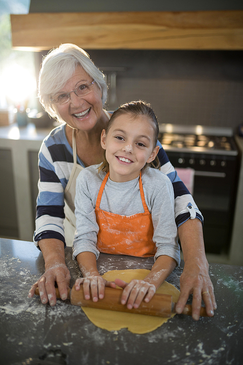 Portrait of grandmother helping granddaughter to flatten dough in the kitchen