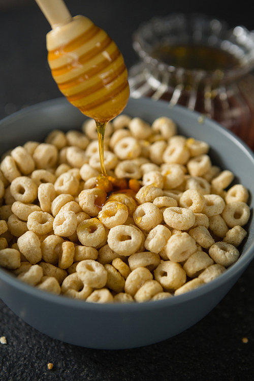 Honey being poured in bowl of cereal rings on black background