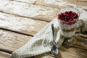 Cup of yogurt muesli and pomegranate with napkin and spoon on table