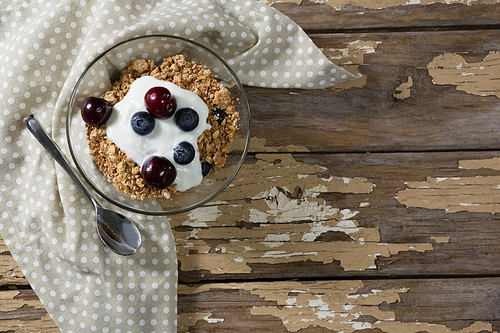 Bowl of yogurt muesli, cherries and blueberries for breakfast on wooden table