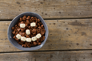 Chocolate cornflakes with honeycomb cereal forming smiley face in bowl on wooden table