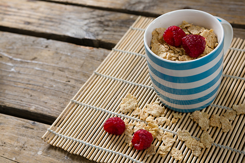 Close-up of flakes with raspberries in mug on place mat