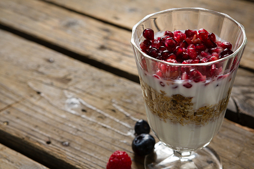 Cup of yogurt muesli and pomegranate for breakfast on wooden table