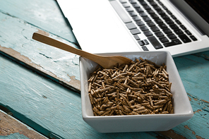 Bowl of cereal bran sticks with spoon and laptop on wooden table
