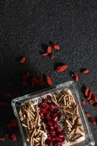 Overhead of yogurt, cereal bran sticks and pomegranate seeds in tray with dried fruits