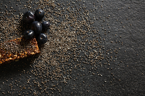 Overhead of granola bar with grains and java plum on black background