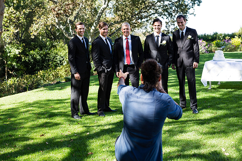 Photographer taking photo of groom and groomsmen at park
