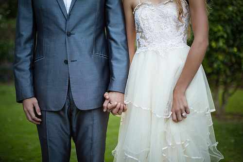 Mid-section of wedding couple holding hands in garden