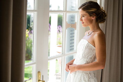 Side view of beautiful bride looking through window while standing at home