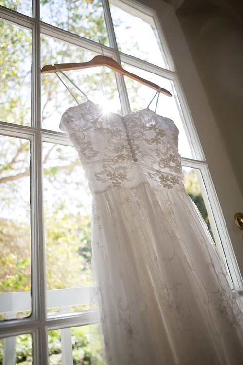 Low angle view of wedding dress hanging on window in dressing room