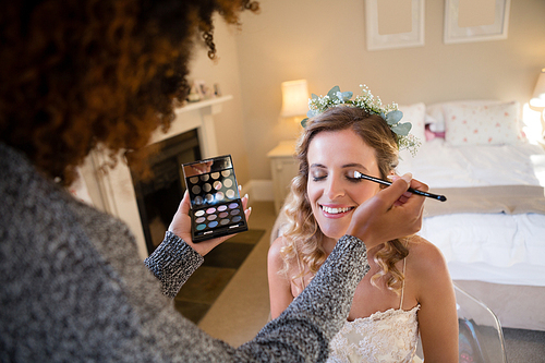 Woman applying makeup to happy bride in dressing room