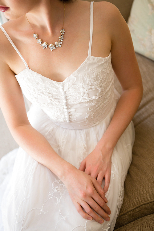 High angle midsection of beautiful bride wearing necklace sitting on sofa at home