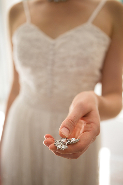 Midsection of bride holding necklace while standing at home