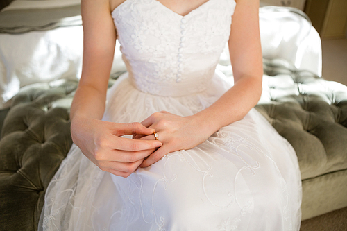 Midsection of bride trying wedding ring while sitting on bed at home