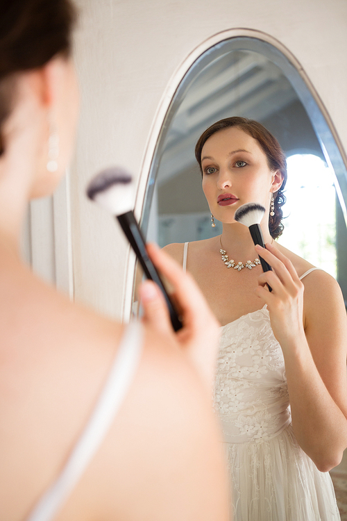 Rear view of beautiful bride applying makeup reflecting on mirror at home