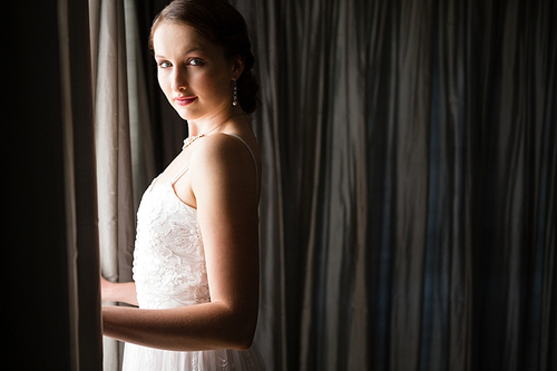 Portrait of beautiful bride standing by window in darkroom at home